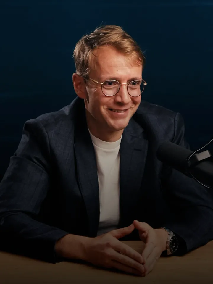 Thibaut Vanderhofstadt in a jacket, smiling, behind a microphone.