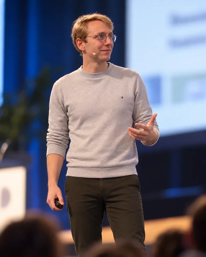 Thibaut Vanderhofstadt on stage with a headset microphone, in front of an audience.